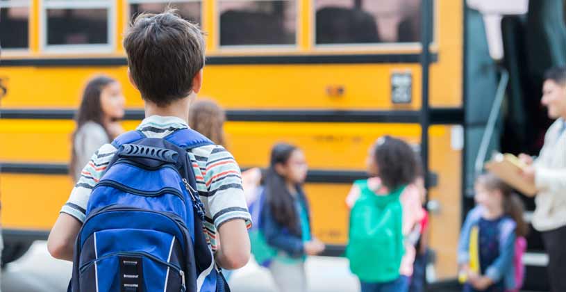 kid wearing back pack in line for school bus