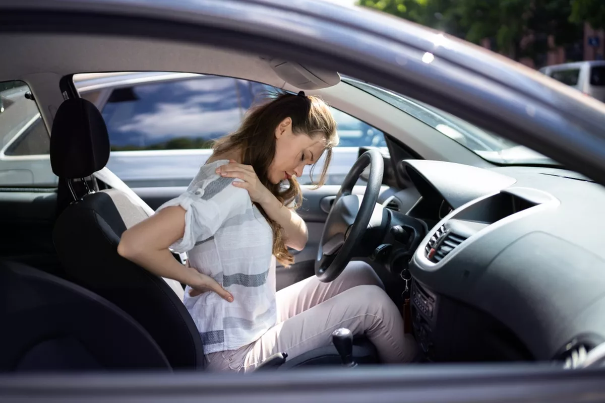 A driver holds her shoulder and back following an automotive accident.